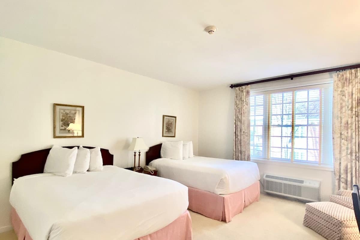 Une chambre d’hôtel avec deux lits, une fenêtre avec des rideaux, une table de chevet avec une lampe et une chaise.