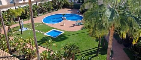 Un patio de hotel con piscina, palmeras y un pequeño jardín.