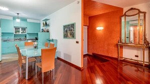 A modern kitchen with teal cabinets, a dining area with a glass table, and a hallway with a mirror and wooden flooring. - Appartamento Magnifico - Porta Venezia  (Milan)