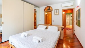 A bedroom with a bed, a wooden nightstand, a mirror, and a door leading to another room. - Appartamento Magnifico - Porta Venezia  (Milan)