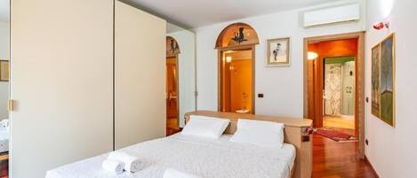 A bedroom with a bed, a wooden nightstand, a mirror, and a door leading to another room.