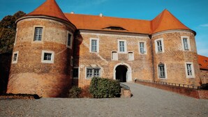 A historic brick building with a central arched entrance, two round towers with conical roofs, and a paved courtyard. - Die Burg (Bad Belzig)
