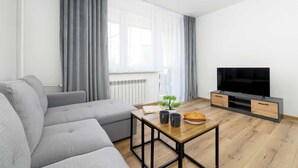 Ein modernes Wohnzimmer mit einem grauen Sofa, einem Holztisch, einem Flachbildfernseher und einem kleinen Topfpflanzen.
