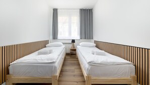 Ein Zimmer mit zwei Holzbettgestellen, einem kleinen Tisch und einem Fenster mit Vorhängen.