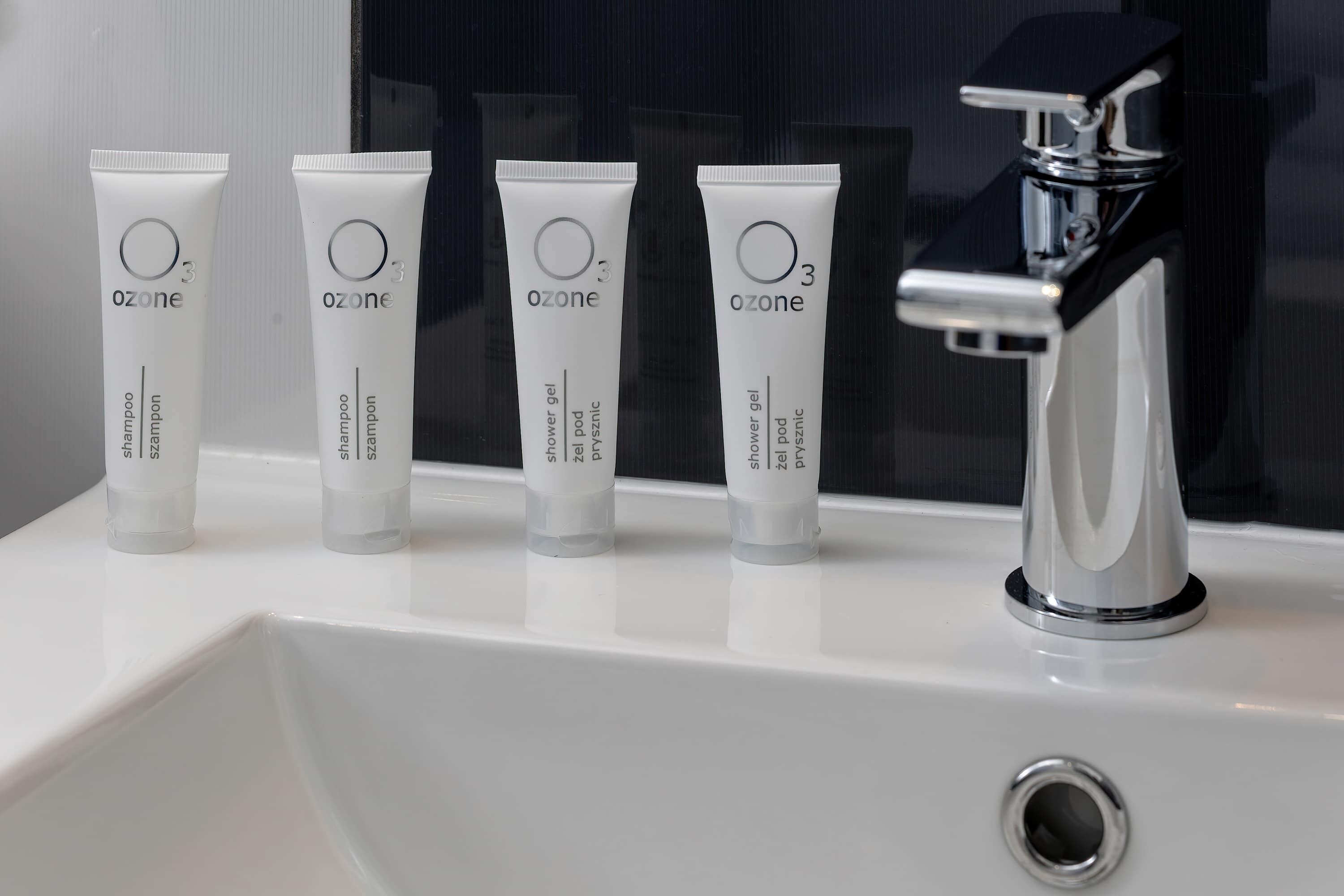 Fire shampoo-tuber fra Ozone på en hvid vask ved siden af et kromarmatur.
