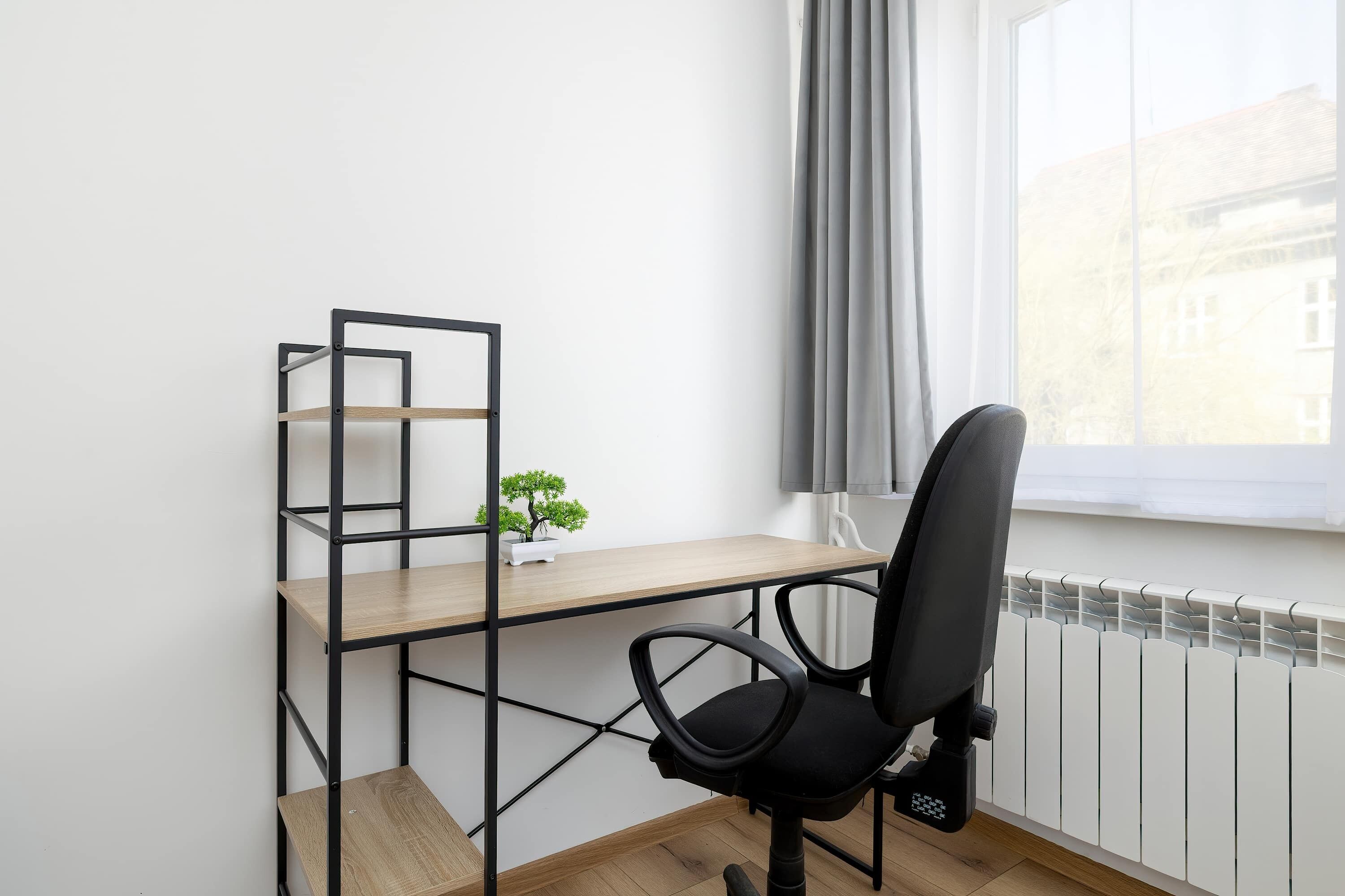 A workspace with a desk, chair, and shelving unit, a small potted plant, and a window with curtains.