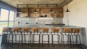 Een moderne keuken met een centraal eiland, barkrukken, hanglampen en uitzicht door grote ramen.