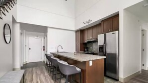 Eine moderne Küche mit Kochinsel, Barhocker, einem Edelstahl-Kühlschrank und Holzschränken.