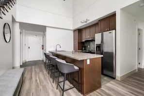 A modern kitchen with a central island, bar stools, a stainless steel refrigerator, and wooden cabinets. - Lakeview Splendor- 7-BR Penthouse Bliss Rooftop (Harrison Hot Springs)