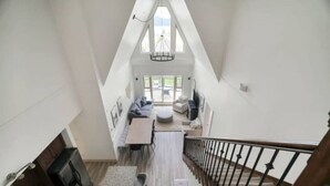 Ein Zimmer mit hohen Decken, einer Wendeltreppe, einem Essbereich mit Tisch und Stühlen sowie einer Sitzecke mit Sofas und einem runden Tisch.