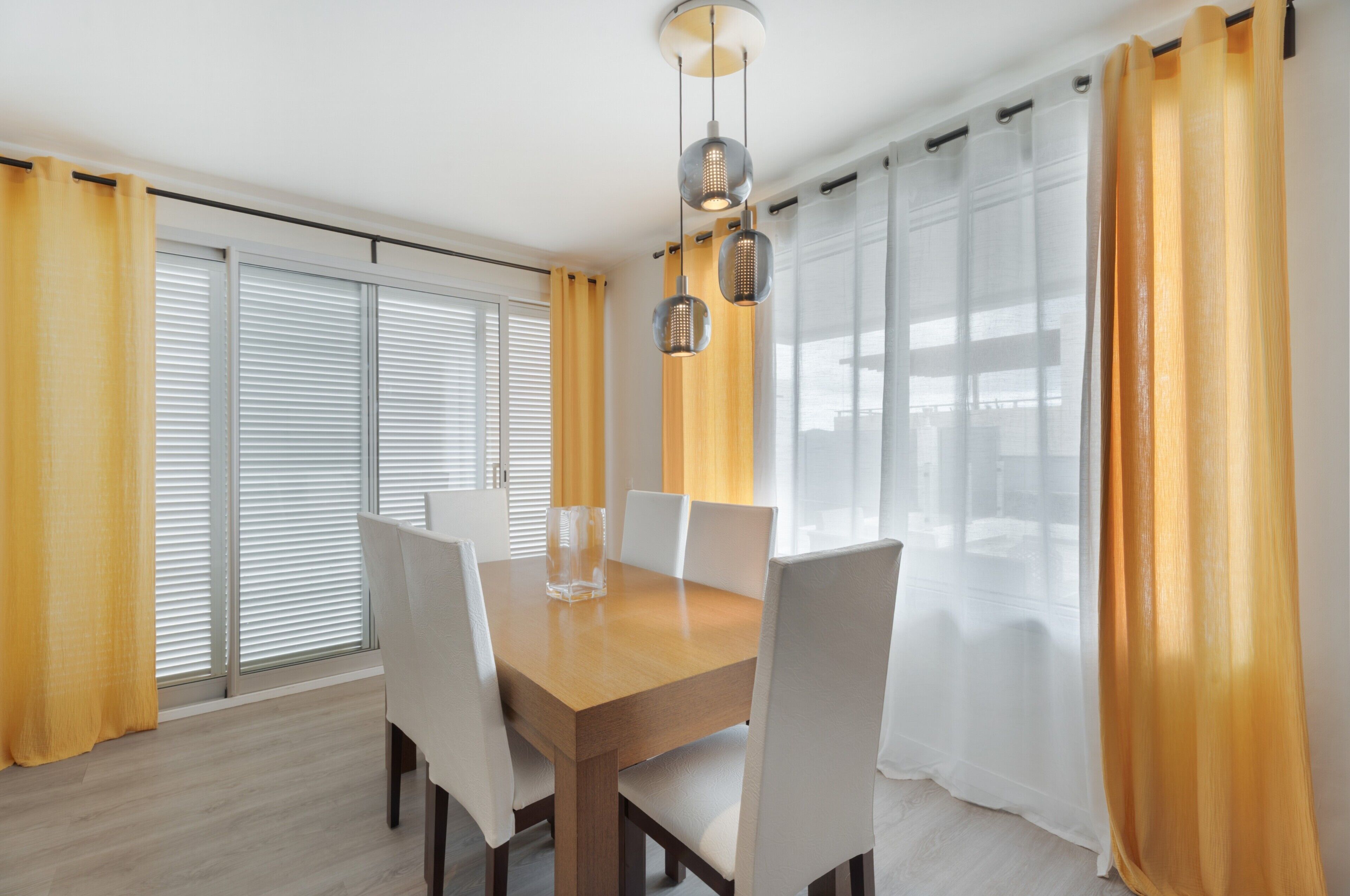 A dining area with a wooden table, white chairs, and a hanging light fixture.