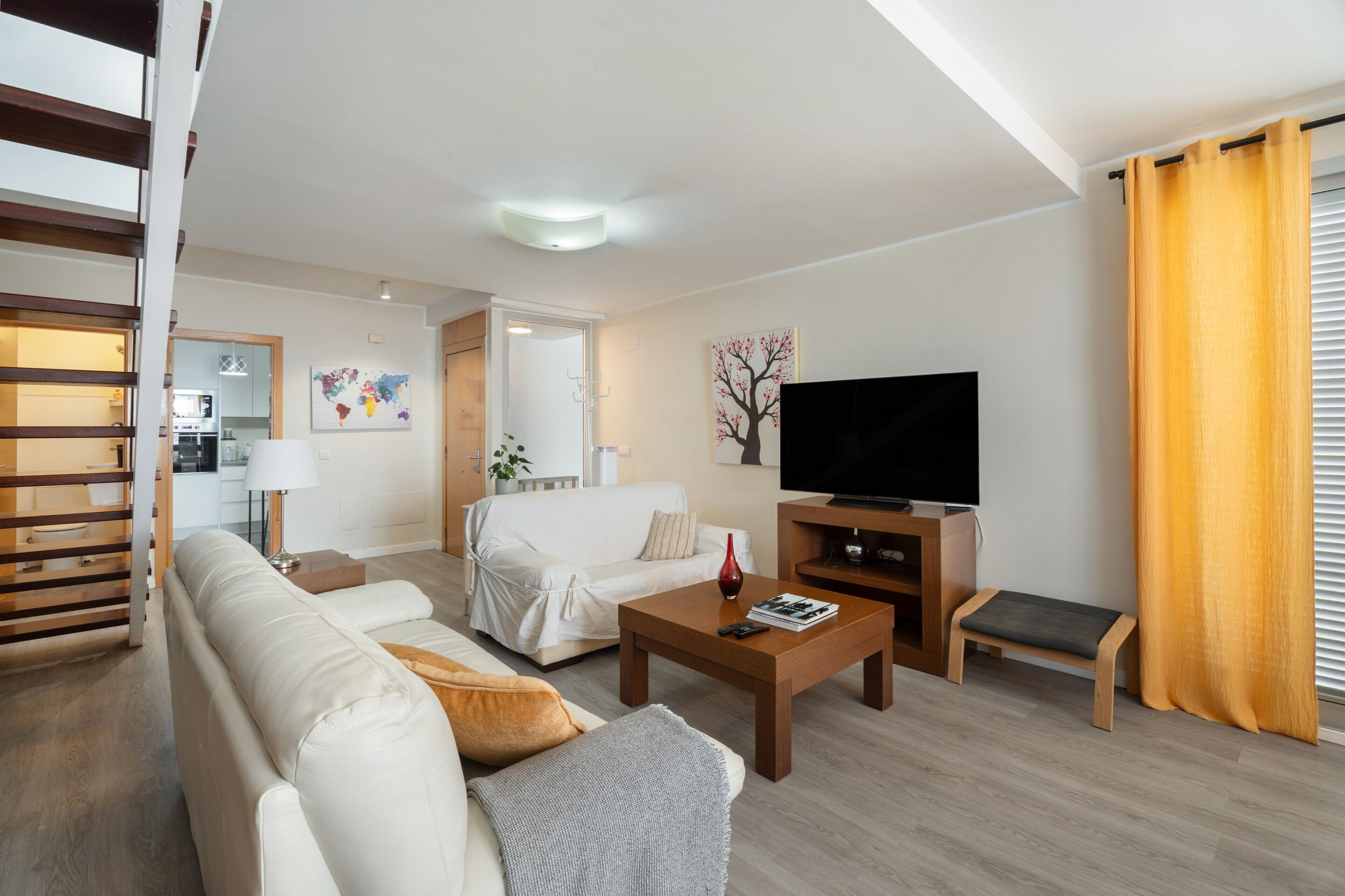 A modern living room with a sofa, coffee table, TV, and a staircase.