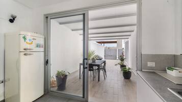 A modern kitchen with a refrigerator, a dining area with chairs and a table, and a sliding glass door leading to an outdoor space.