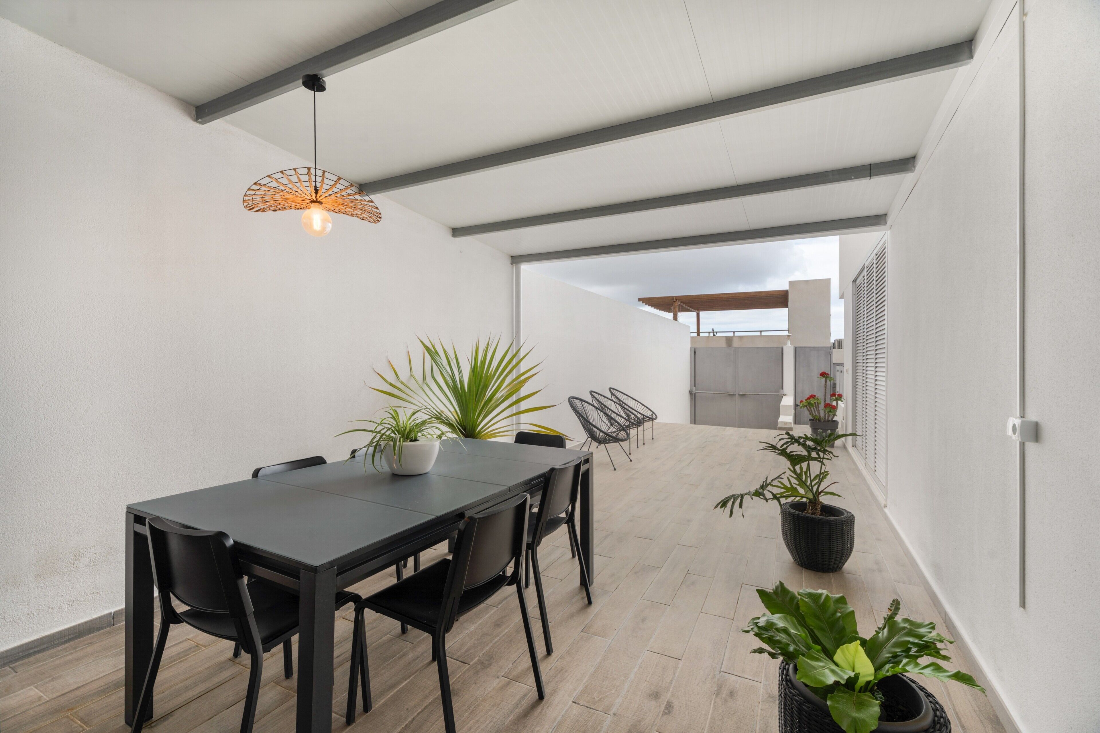 A modern dining area with a long table, black chairs, potted plants, and a hanging light fixture.