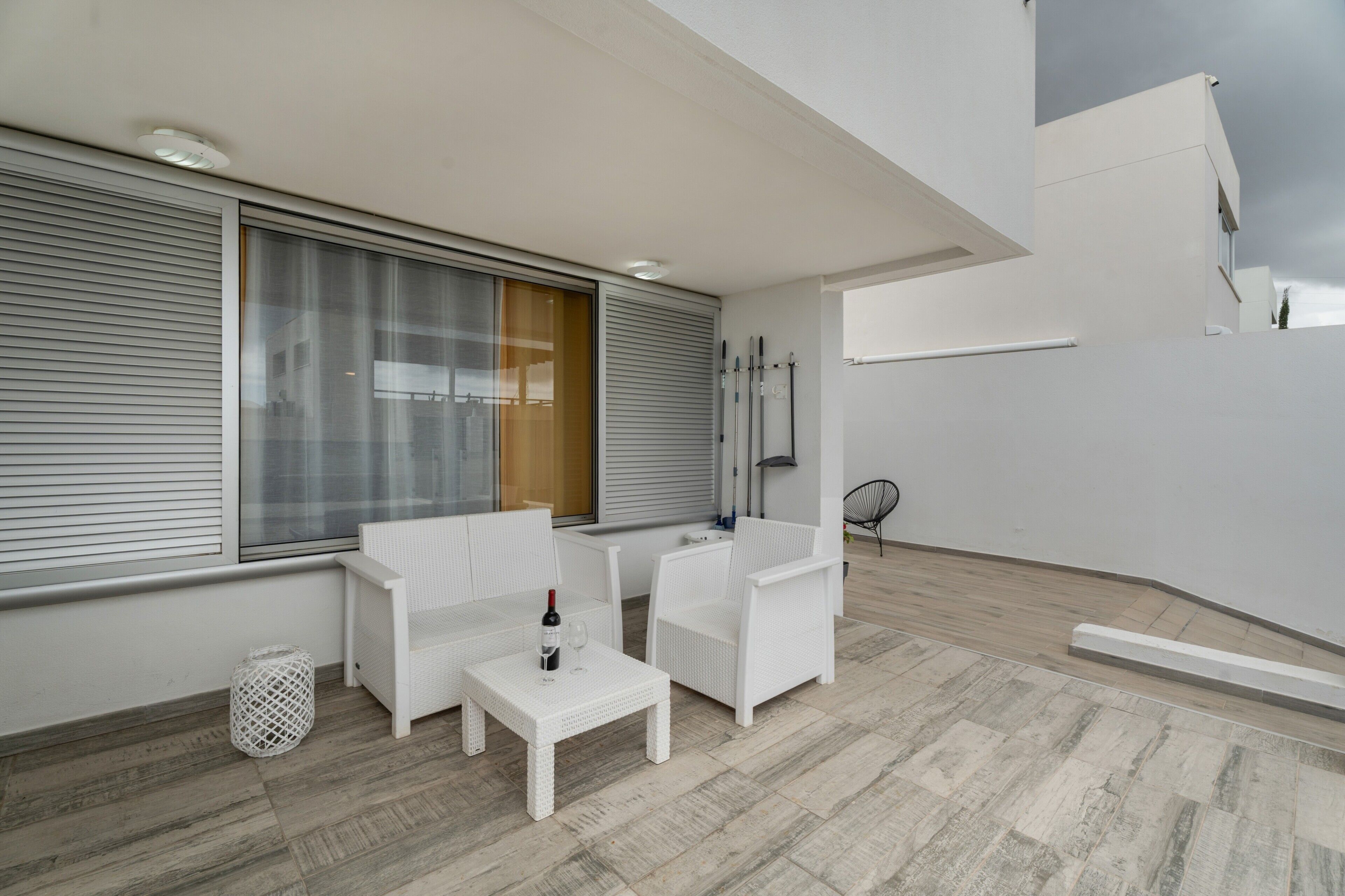 Een balkon met witte meubels, een tafel met een fles en glas, en uitzicht op de stad.