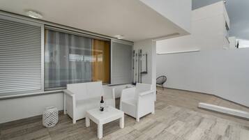 Een balkon met witte meubels, een tafel met een fles en glas, en uitzicht op de stad.