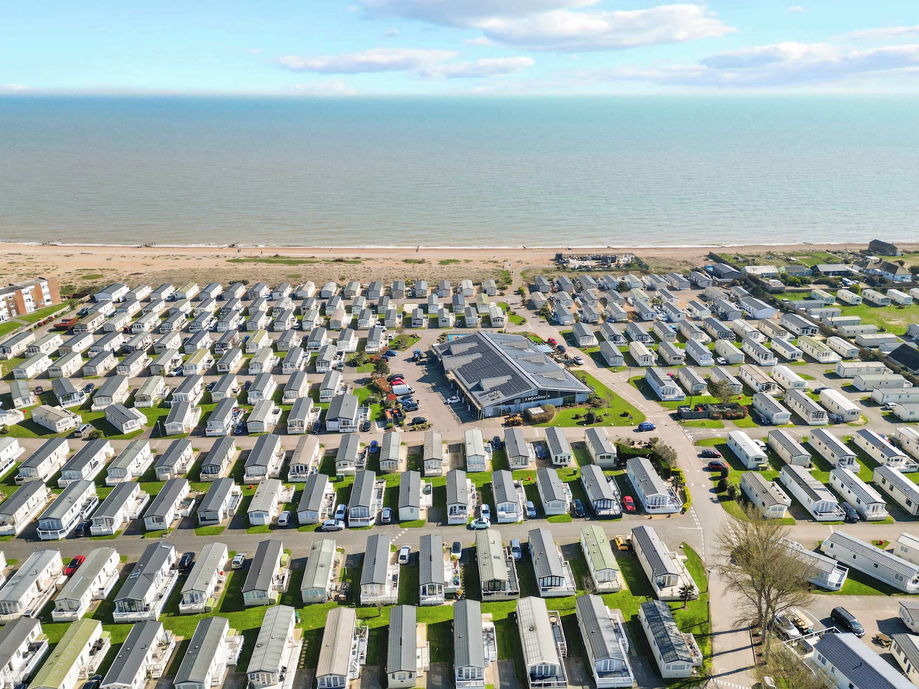 Un extenso parque de caravanas con filas de vehículos, un edificio central y una playa al fondo.