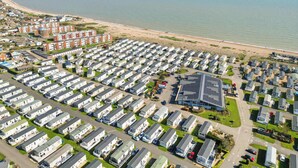 A coastal caravan park with rows of caravans, a beach, and a residential area with houses. - Charming Beachside Chalet close to clubhouse (Pevensey Bay)