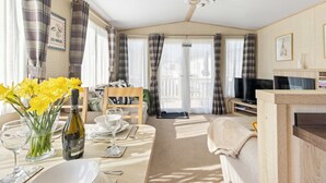 A cozy living room with a dining area, a television, and a fireplace. - Charming Beachside Chalet close to clubhouse (Pevensey Bay)