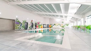 An indoor swimming pool with a tiled floor, surrounded by green chairs and tables, and walls decorated with floral murals. - Charming Beachside Chalet close to clubhouse (Pevensey Bay)