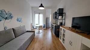 Kompakti olohuone, jossa on sohva, ruokapöytä, tuolit, televisio ja keittiökaapit.