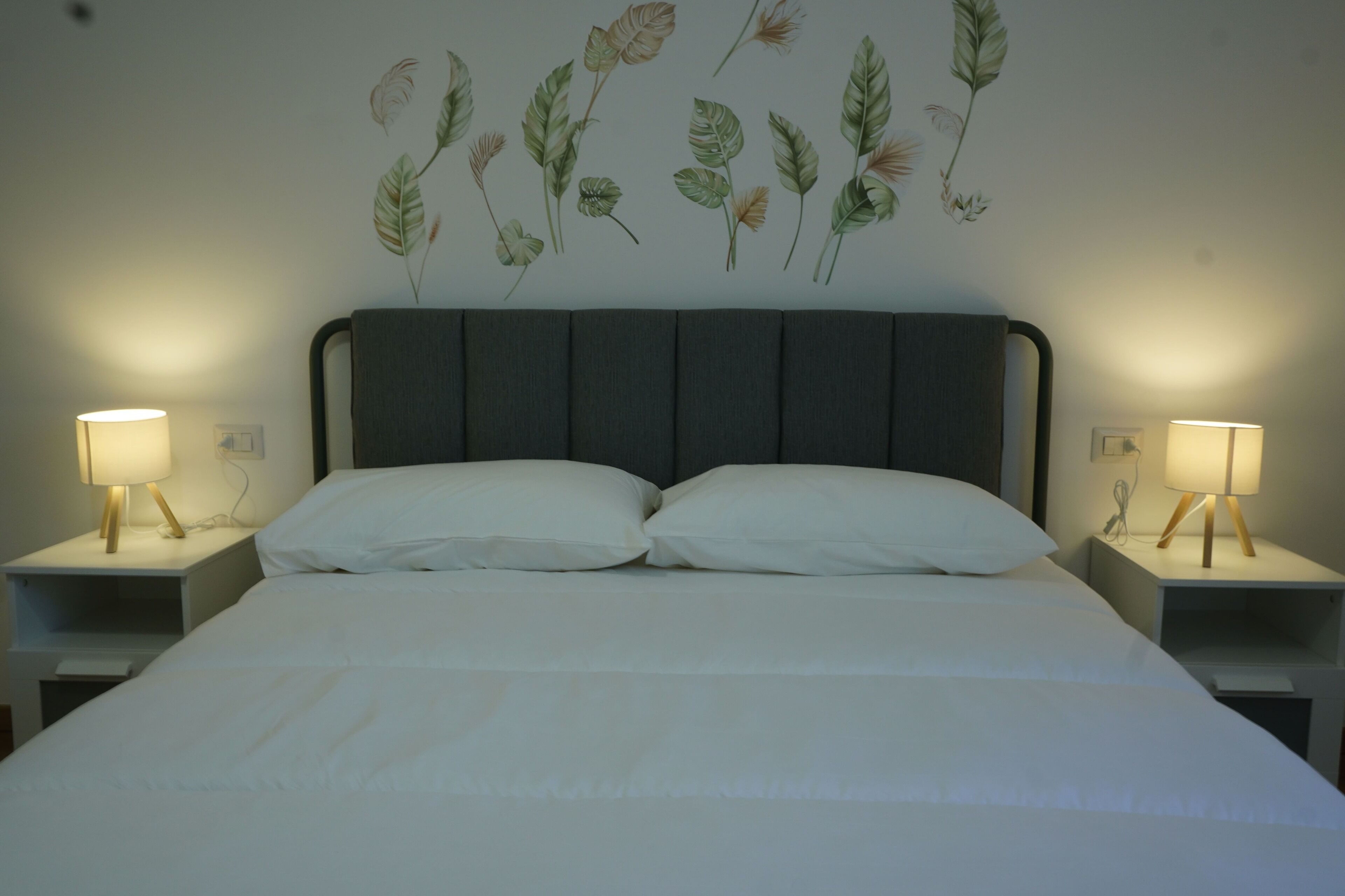 A bed with two pillows, flanked by two bedside tables with lamps, in a room with a wall-mounted botanical print.
