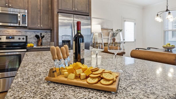 Une cuisine avec des plans de travail en granit, une bouteille de vin, du fromage et des crackers.