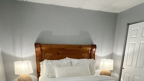 A bedroom with a wooden headboard, two bedside lamps, a white bedspread, and a door to the right. - Newly Furnished St. Charles Getaway- B (Saint Charles)