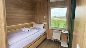 Een eenpersoonsbed met houten hoofdbord, een raam met uitzicht op groen en een wandgemonteerde airconditioning.