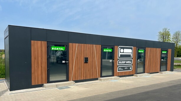 Een modern hostel met meerdere kamers, elk aangeduid met een bordje 'ROATEL', en een bord 'SLEEP WELL' dat wijst op een initiatief voor een goede nachtrust.