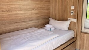 Een enkel bed met wit beddengoed, een houten hoofdbord en een raam met zonwering.