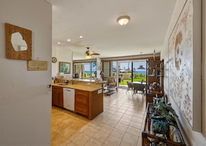A spacious kitchen with a large island, a dining area with a view, and a living area with a ceiling fan. - NEW! Oceanfront Maui Retreat at Napili Point - Unit B16 (Lahaina)
