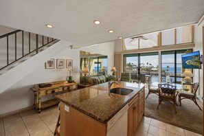 A spacious kitchen with a granite countertop, wooden cabinets, and a large island. - NEW! Oceanfront 2BR Loft with Sunset Views - Unit C23 (Lahaina)