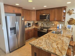 A kitchen with granite countertops, stainless steel appliances, wooden cabinets, and a stone backsplash. - NEW! Napili Point Oceanfront Family Loft - Unit C4 (Lahaina)