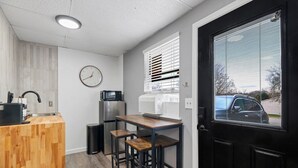 A compact kitchen with a wooden counter, a refrigerator, a microwave, a sink, and a clock on the wall.