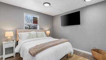 A modern bedroom with a bed, nightstands, a TV, and a window with blinds.