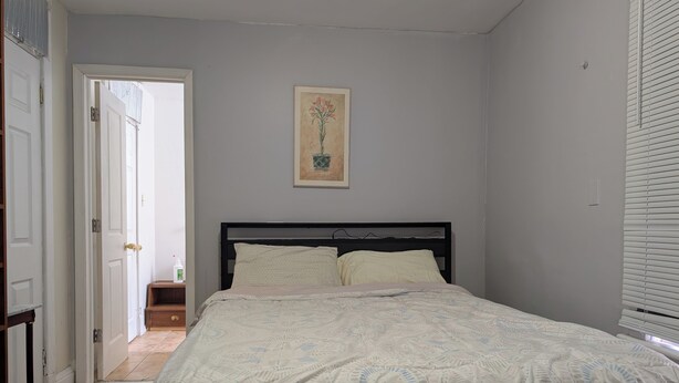 Une chambre à coucher avec un lit, une porte donnant sur une autre pièce, une petite table avec une bouteille et un tableau accroché au mur.