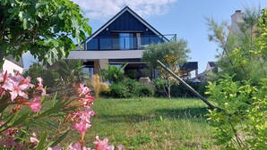 Une maison moderne dotée d’un grand balcon, entourée d’une végétation luxuriante et de plantes en fleurs.