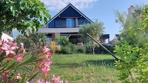 Ein modernes Haus mit einem großen Balkon, umgeben von üppigem Grün und blühenden Pflanzen.