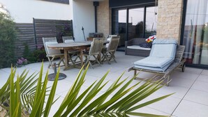 Une terrasse extérieure avec une table ronde en bois, quatre chaises, un canapé et un fauteuil de relaxation.