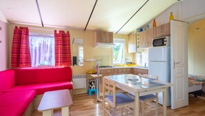 A compact living space with a kitchenette, a dining area, and a seating area. - Mobile Home Near Royan with Shared Pool, Private Terrace, and Wi-Fi (Meschers-sur-Gironde)