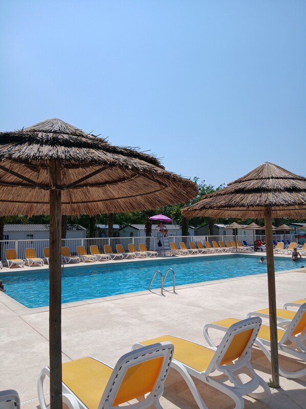 Zwembad met ligbedden en rieten parasols.
