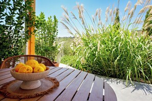 Une table en bois sur laquelle se trouve un saladier rempli de citrons, une chaise en osier et, au fond, de hautes herbes.