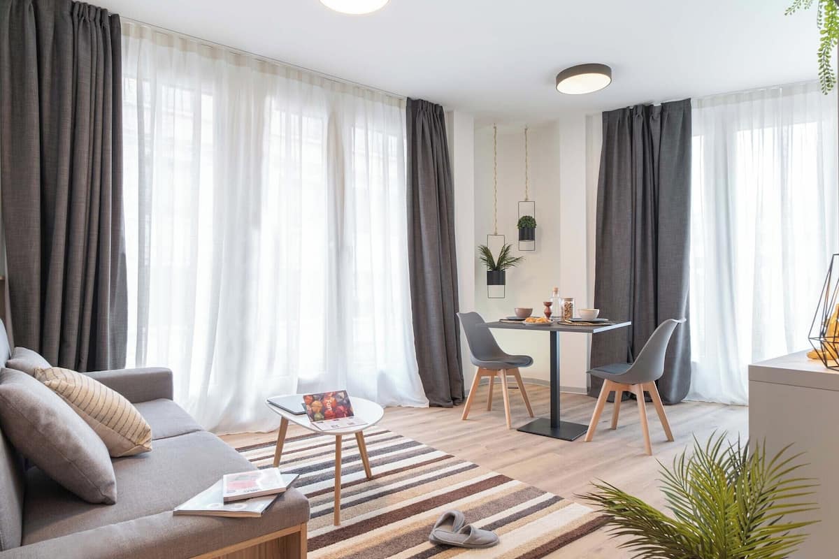 A modern living room with a sofa, a coffee table, a dining table with chairs, and a kitchen area in the background.