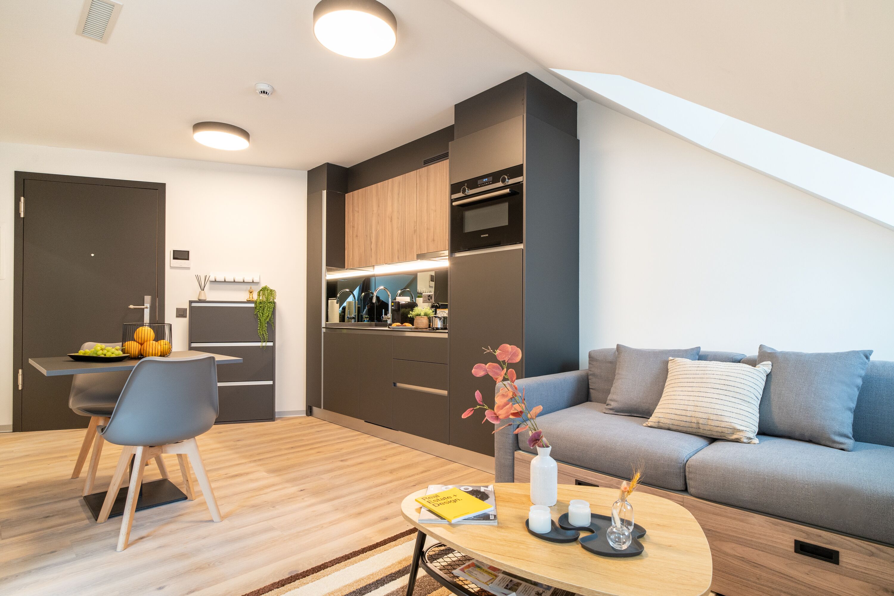 A modern living space with a dining area, kitchenette, and a sofa with cushions.