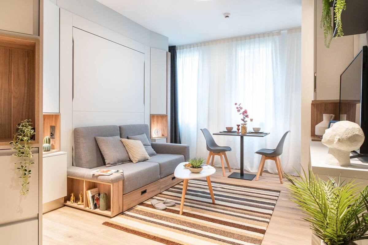 A modern living room with a sofa, a small table, chairs, a coffee table, and a large window with curtains.