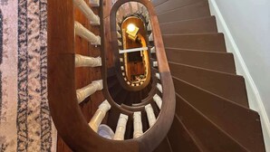Una escalera de caracol de madera con barandillas blancas, que conduce a un rellano con una lámpara.