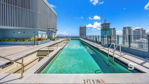 Une piscine sur le toit offrant une vue sur la ville, un bâtiment moderne aux lignes verticales et un ciel d’un bleu limpide.