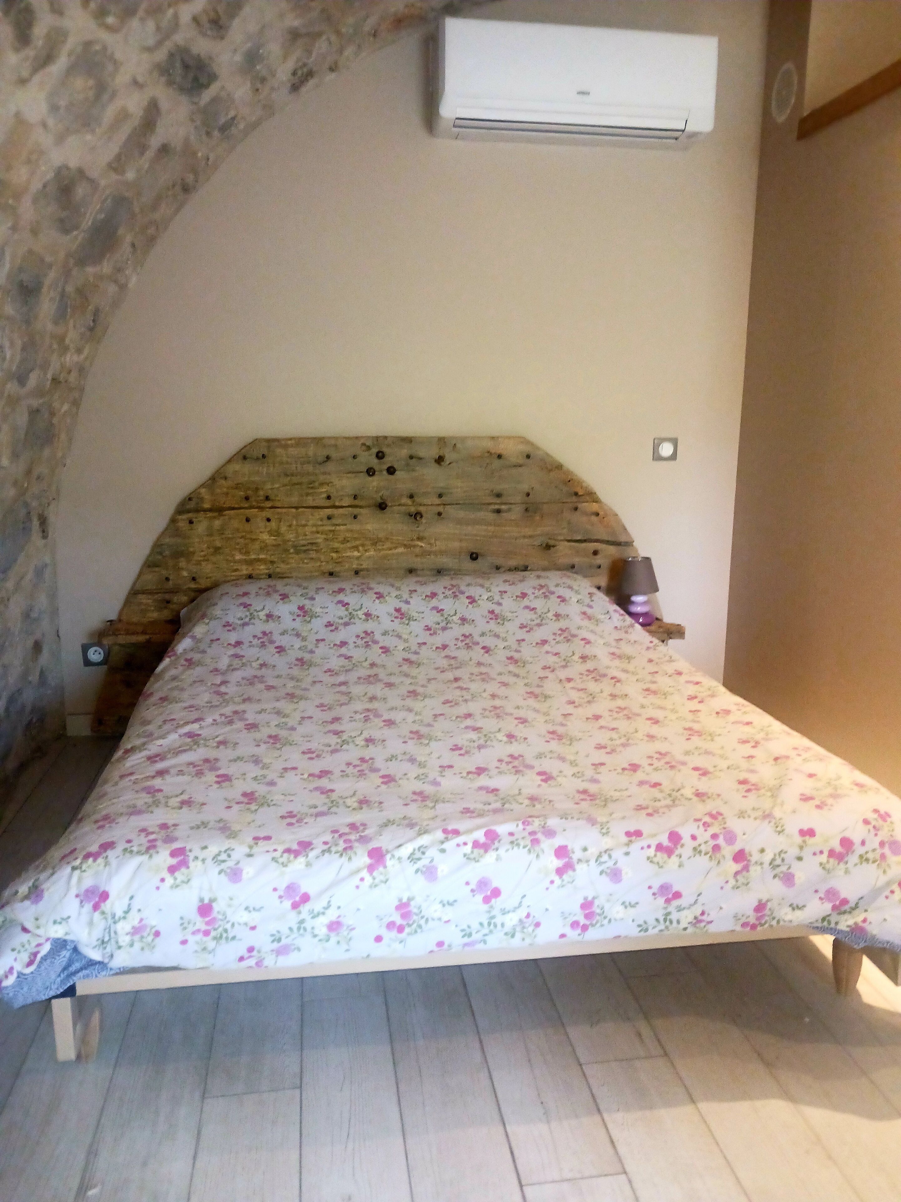 Une chambre à coucher avec une tête de lit en bois, une couvre-lit à motifs floraux et un climatiseur fixé au mur.