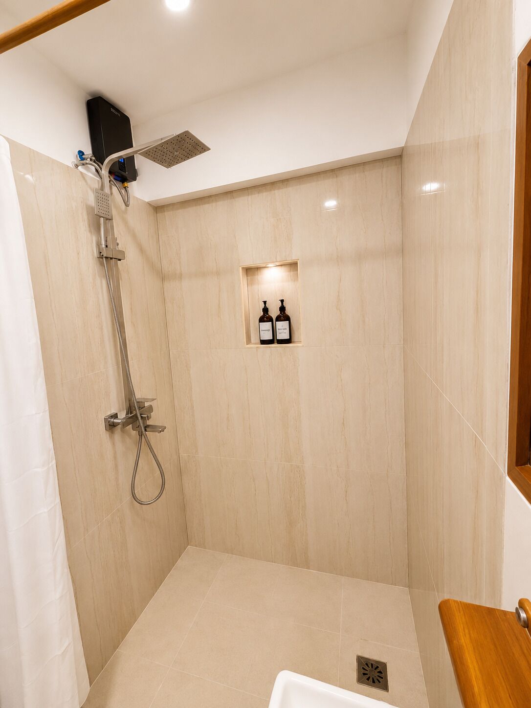 A shower with a handheld showerhead, a wall-mounted control panel, and a small shelf with two bottles.